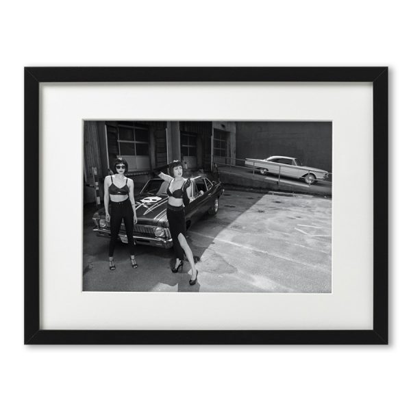 Foto-Print Oberhafen-Zyklus No. 02 auf Ilford S/W-Papier, gerahmt. Cars & Girls Fotografie von Carlos Kella im Format 21 x 31 cm mit Passepartout und Rahmen. Sophie Bolvary & Laura Desirée und eine Chevy Nova,1972 im Hamburger Oberhafen.